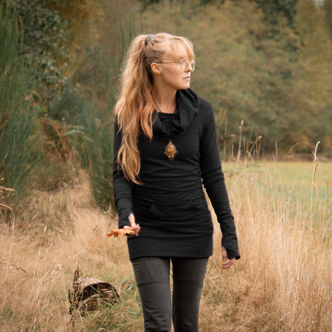 Woman in a black outfit standing in a field with trees in the background
