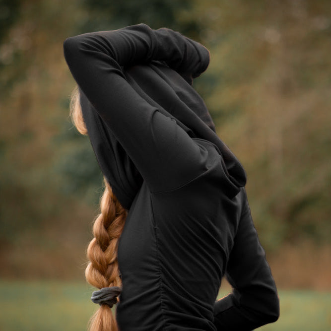 Person wearing a black hooded swearer with braided hair, standing in a natural setting.