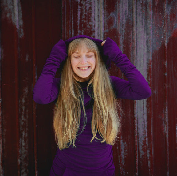 Person wearing a purple outfit in front of a red and gray textured wall