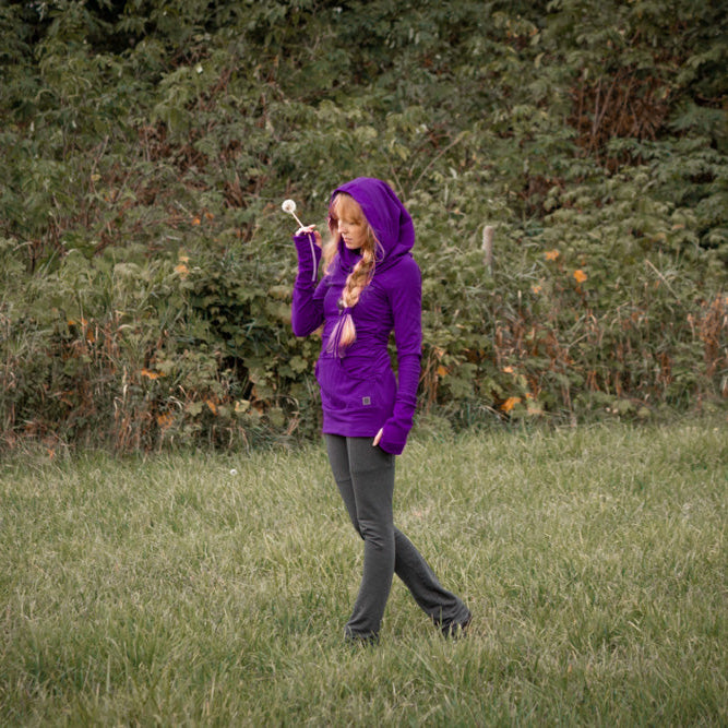 Person wearing a purple sweater standing in a grassy field with trees in the background