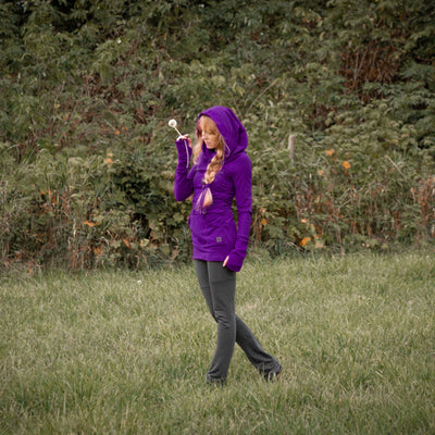 Person wearing a purple sweater standing in a grassy field with trees in the background