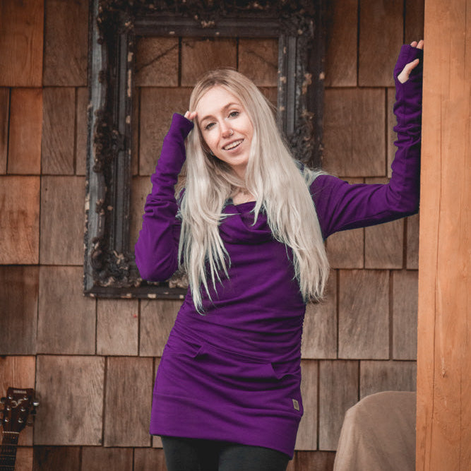 Woman in a purple sweater standing in front of a wooden wall.