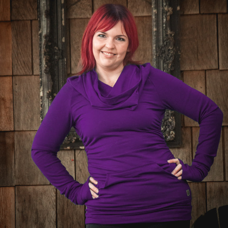 Woman wearing a purple sweater standing in front of a wooden wall.