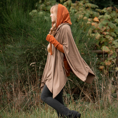 Person wearing a mocha Tulu poncho and a Rust Goddess Sweater walking through a forest.
